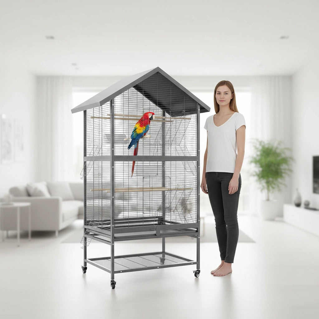 Femme présentant une imposante cage perroquet xxl grise à toit en forme de maison avec grand Ara sur son perchoir