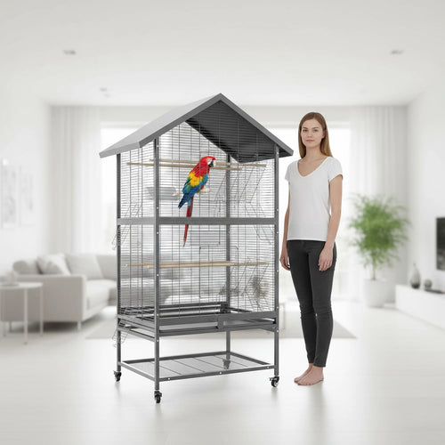 Femme présentant une imposante cage perroquet xxl grise à toit en forme de maison avec grand Ara sur son perchoir